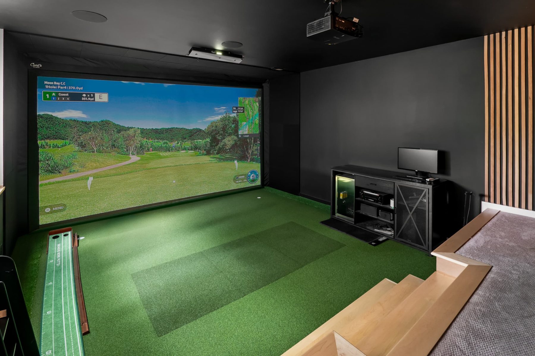 Basement golf simulator with a putting strip and wood-slat accent wall